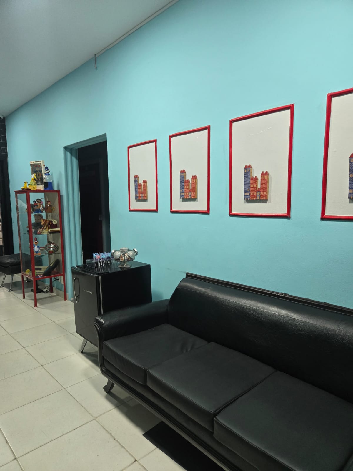 Sala de espera com sofá preto, quadros e estante de brinquedos retrô